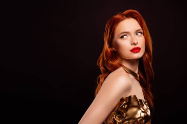 Altın rengi elbise giyen şık, kızıl saçlı bir kadın, koyu bir arka planda zarif bir şekilde duruyor. İfade eden makyaj onun ışıltılı cazibesini ve cazibesini arttırıyor..