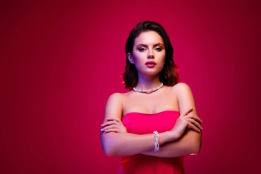Pembe elbise ve inci aksesuar giyen şık bir kadın moda ve görkemli bir atmosfer için canlı renkli ışıkta rahatça poz veriyor.