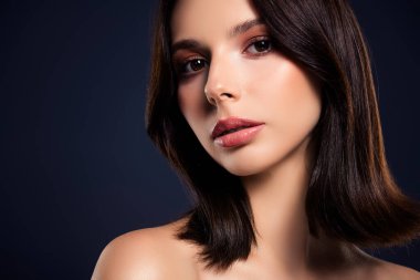 Genç esmer bir kadının yakın çekimi pürüzsüz bir ten, nazik bir makyaj ve koyu mavi arka plan doğal zarafet ve güzellik sergiliyor..