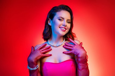 Zarafet ve cazibe saçan zarif bir bayan pembe bir elbise, eldiven ve inci takılar giyer. Parlak kırmızı arka plan, onun büyüleyici ve sofistike cazibesini vurguluyor..