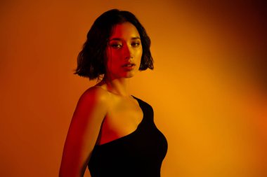 Şık bir elbise giymiş, modern ve büyüleyici bir cazibe için sıcak, gradyan aydınlatma ile yıkanmış kısa esmer saçlı şık bir genç kadının portresi..