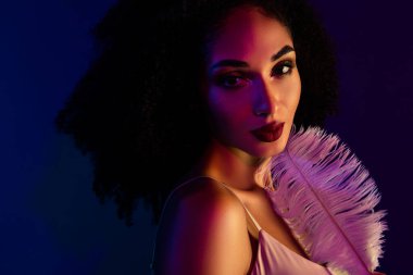 Kıvırcık siyah saçlı, parlak neon renklerle aydınlatılmış, modern bir ortamda güzellik, tarz ve duygusallığı ifade eden genç bir kadının yakın çekimi.