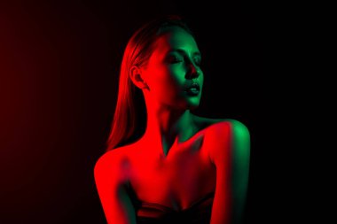 Kırmızı ve yeşil neon ışıkla yıkanmış genç bir kadının büyüleyici görüntüsü, koyu bir arka plana karşı bir stil ve modern zarafet hissi uyandırıyor..