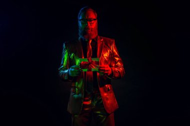 Parlak takım elbiseli sakallı bir adam esrarengiz bir hediye tutar, parlak neon ışıklarla aydınlatılır, koyu siyah bir arka plana karşı, zarafet ve gizem saçar..