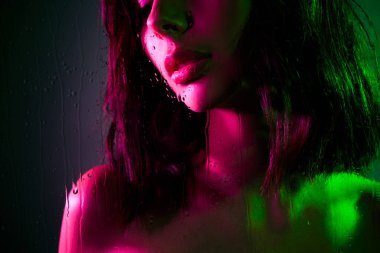 Pembe ve yeşil neon ışıklarla aydınlatılmış, büyüleyici ve modern bir estetik sergileyen güzel bir genç kadın. Karmaşık ışık oyunu gizemli ve sanatsal atmosferi güçlendirir..