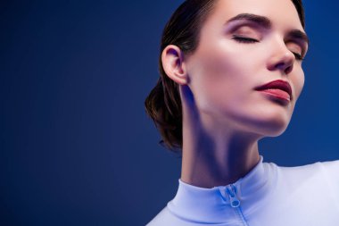 Aerodinamik beyaz bir elbise içinde zarif bir genç kadın, zarif bir makyajı var. Çağdaş mavi arka planda poz vermek, güzellik, entelektüellik ve modern tarzı yansıtır..