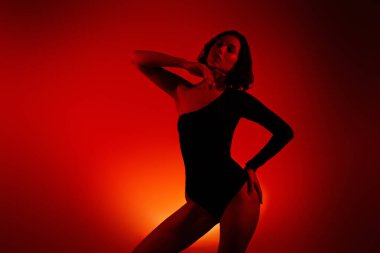 Turuncu ve sarı arka planda şık pozlar veren genç bir kadın. Büyüleyici ifadesi ve sanatsal sunumu, canlı, ışıltılı bir sahnede moda ve güzelliği yansıtıyor..