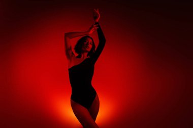 Şık bir tek omuzlu vücut giysisi içinde zarif bir genç kadının sanatsal tasviri. Sıcak renklerdeki çarpıcı aydınlatma gradyanı onun güzelliğini vurguluyor ve çağdaş sanatsal bir dokunuş ekliyor..