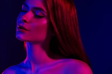 Kızıl saçlı ve kusursuz hatlara sahip genç bir kadın, canlı neon ışıkla aydınlatılmış, çağdaş güzellik, moda zerafeti ve sanatsal ifade temalarıyla iletiliyor..