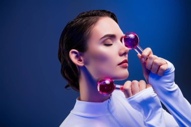 Fütüristik bir stüdyoda genç bir kadın canlı neon ışıkları, somut güzellik, modern tarz ve lüks kişisel bakım kavramları altında yüz bakımı rutini uyguluyor..