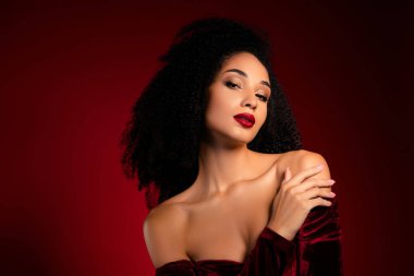 Dalgalı kıvırcık saçlı kadın omuzlarına dokunuyor. Kırmızı kadife elbise giyince çok çekici oluyor..