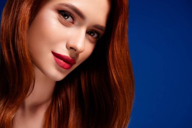 Kırmızı saçlı, çarpıcı makyajlı, güzelliğini ve tarzını vurgulayan, mavi arkaplana dayanan bir kadının yakın plan portresi..