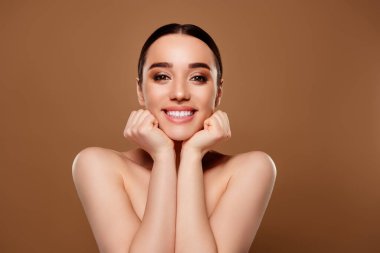 Güzel, mutlu, çıplak bir kadının, bej renkli arka planda izole edilmiş cazibeli makyajın keyfini çıkardığı fotoğraf..