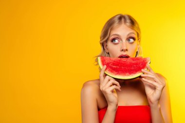 Güzel kız modelin fotoğrafı boş uzay ısıran karpuz dilimi sarı pastel arka planda izole edilmiş..
