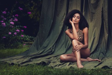 Yeşil bir giysinin üzerinde doğal saçlı, zarif bir genç kadının portresi, yemyeşil bir arka planda güzel ve özgüvenli bir şekilde oturuyor..