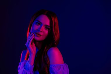 Genç bir kadının çarpıcı görüntüsü, kırmızı ve mavi ışığın gradyanı karşısında zarif özelliklerini, şık görünümünü ve canlı görüntüsünü vurguluyor..