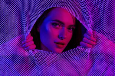 Çarpıcı bir fotoğraf, modern moda, güzellik ve sanatsal ifadeyi vurgulayan parlak mavi ve pembe ışıkla aydınlatılmış örgülerin arkasında genç ve güzel bir kadını gösteriyor..