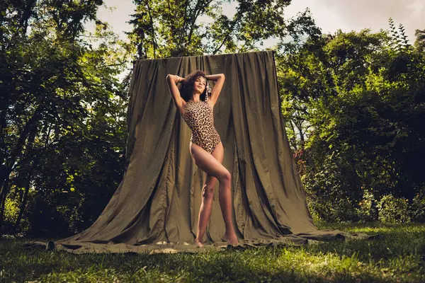 Dışarıda poz veren leopar desenli bir kadın. Sahne güzelliği, doğayı ve modaya uygun tarzını sergiliyor, kendine güveni ve zarafeti vurguluyor, verimli, güneşli bir park atmosferinde..