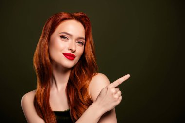 Hassas, nazik, çarpıcı zengin bir kadının, haki rengi arka planda izole edilmiş boş bir parmak gösteren fotoğrafı..