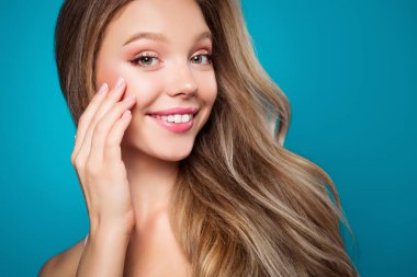 Görüntü, parıldayan doğal bir güzelliğe, açık makyaja, çarpıcı sarı saçlara ve parlak mavi bir arka plana sahip büyüleyici bir ifadeye sahip genç bir kadını yakalıyor..