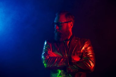 Parlak takım elbiseli karizmatik bir adam neon mavi ve kırmızı ışıklarla aydınlatılır ve canlı ve şık bir atmosfer yaratır..