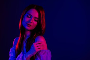 Sanatsal ışıklandırma, cazibe, güzellik ve kendine güven temalarıyla aydınlatılmış, kendine güvenen, mavi arka planda duran genç bir kadının büyüleyici görüntüsü..