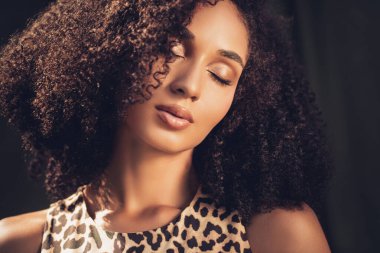 Büyüleyici genç bir kadın, doğal güzelliğini ve kıvırcık saç stilini göstererek zamansız ve zarif bir portre yaratıyor.