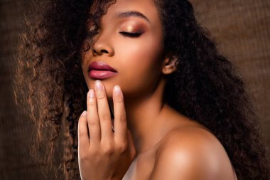 Doğal kıvırcık saçlı, zarif makyajlı, ışıl ışıl ciltli, güzelliği, zarafeti ve kendine güveni olan büyüleyici bir yakın çekim. Yumuşak, kahverengi arka plan onun büyüleyici yüz ifadesine odaklanmasını sağlar..