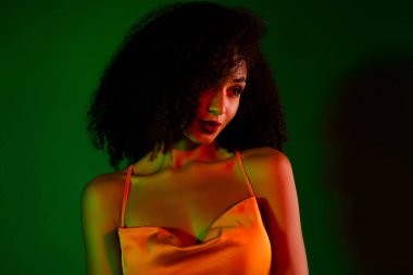 Göz kamaştırıcı özellikleri olan şık bir model canlı ışıklandırma altında şık turuncu bir elbise giyiyor, bir stüdyo fotoğrafçısında sofistike ve büyüleyici bir görüntü yayıyor..