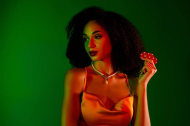 Modaya uygun genç bir kadın, canlı bir geçmişe karşı poker fişi taşıyor, kendine güveni ve lüksü var..