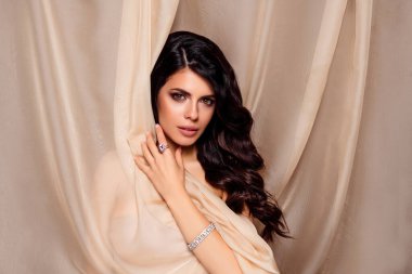 Genç ve güzel bir esmer kadının portresi lüks mücevherler takıyor, bej kumaşla örtülü, zarif ve sofistike.