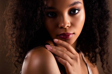 Büyüleyici bir portre, kıvırcık siyah saçlı, etkileyici gözleri olan, zarafet ve güzellik saçan, sıcak kahverengi arka planda, doğal cazibe ve zarafeti vurgulayan,.