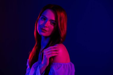 Zarif pozlara sahip genç bir kadın, çağdaş bir stüdyo moda portresindeki güzelliğini, tarzını ve sofistikesini vurgulayarak, kırmızı ve mavi ışıkla aydınlanıyor..