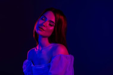 Canlı kızıl saçlı genç bir kadın dramatik kırmızı ve mavi ışıklar altında parıldıyor, güzel, zarif ve sakin bir ifade, cildini, kadınlığını ve modasını ön plana çıkarıyor..