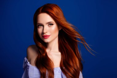 Akan kızıl saçları ve kusursuz makyajıyla çarpıcı genç bir kadın zarif mavi bir arka plana karşı zarif bir şekilde poz veriyor, güzel ve zarif bir şekilde..