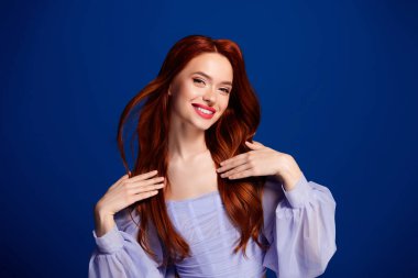 Kızıl saçlı genç bir kadının canlı bir portresi canlı mavi bir arka plana karşı güvenle poz veren, zarafet, tarz ve kadınsı güzelliğin vücut bulmuş hali..