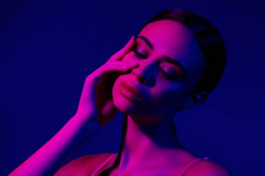 Ultraviyole ışıkla aydınlatılmış, güzelliğini vurgulayan genç bir kadının sanatsal fotoğrafları. Neon mavi ve pembe renkler onun özelliklerinin zıtlığını vurgular ve gece kulübünden esinlenilmiş bir atmosfer yaratır..