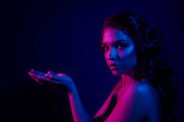 Göz kamaştırıcı genç bir kadın canlı neon mavi ve pembe ışıkla yıkanmış, şehvetli zarafet ve güzellik sergiliyor, stil ve sanatsal ifadeler için mükemmel..