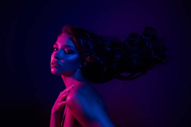 Mavi ve pembe tonlarda neon ışık altında poz veren genç bir kadının portresi büyüleyici ve sanatsal bir sahne yaratıyor..