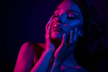 Parlak neon ve pembe ışıklarla aydınlatılmış esmer kadın, göz alıcı ve şık bir görünüm sergiliyor, güzelliği, makyajı ve büyüleyici zarafeti ön plana çıkarıyor..