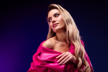 Çekici bir güzelliğe sahip zarif sarışın kadın şık pembe bir trençkot giyiyor modern mor bir arka plana karşı lüks ve zarafet sergiliyor. Şehvetli ve çekici bir havası olan yüksek moda konsepti..