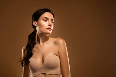 Güzel esmer bir kadının portresi askısız bir bluz giyiyor. Parlak cildini ve doğal güzelliğini sergiliyor. Zarif bir efekt için yumuşak bej bir zemin üzerine kurulmuş..