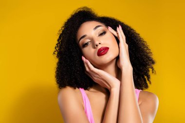 Kıvırcık saçlı, parlak dudaklı, kendine güveni tam genç bir kadın, canlı sarı arka planda poz veriyor, moda, zarafet ve modern estetik..