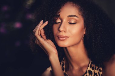 Kendine güvenen, çekici, parlak tenli, kıvırcık saçlı, açık havada huzurlu bir anın tadını çıkaran genç bir kadının yakın çekimi..