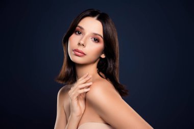 Işıldayan tenini, minimalist makyajını ve dengeli ifadesini gösteren esmer bir kadının zarif portresi, ince bir koyu mavi arka plan, büyüleyici ve sofistike.