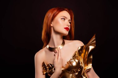 Parlak kızıl saçlı, altın rengi giysili ve sofistike makyajlı, koyu renk bir arka fona kurulmuş zarif bir genç kadın. Görüntü, stil, cazibe ve lüks içerir..