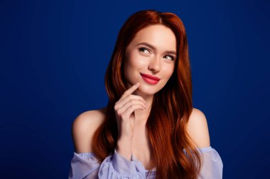 Canlı kızıl saçlı ve kusursuz makyajlı genç bir manken. Stüdyoda zarif bir şekilde poz veriyor. Mavi arka planı var.