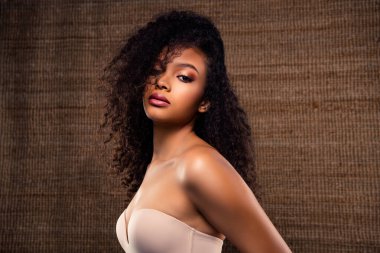 Genç bir kadın modelin zarif portresi doğal cazibesini ve güzelliğini sergiliyor çarpıcı kıvırcık saçları ve göz alıcı makyajı ile rahat bir stüdyo ortamında.