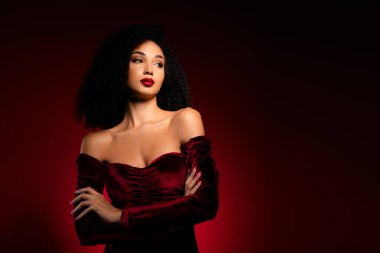 İpeksi gece elbisesi içinde güzel zengin bir kadın kollarını kavuşturmuş boş alana bakıyor..