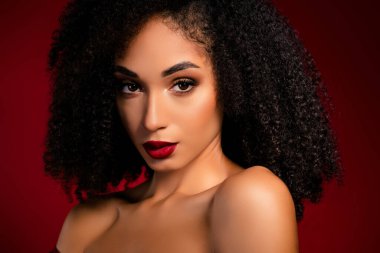 Şık, çekici bir kız, kameraya bakıp kırmızı arka planda parlak, parlak bir makyaj yaparken cilveli hisseder..